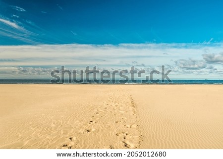 Footprints in the sand leading to to sea in Liepaja, Latvia. Large, empty beach with fine white sand over blue sky; popular holiday destination. Latvian landscape captured in a sunny autumn day.  Royalty-Free Stock Photo #2052012680