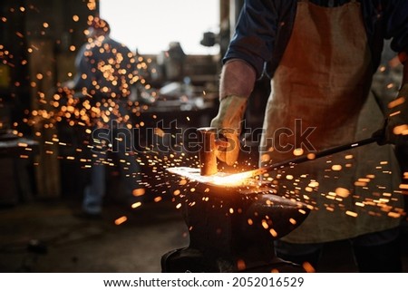 Close-up of blacksmith in apron working with hammer and iron in the workshop Royalty-Free Stock Photo #2052016529