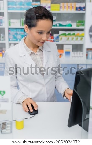 pharmacist in white coat using computer in drugstore
