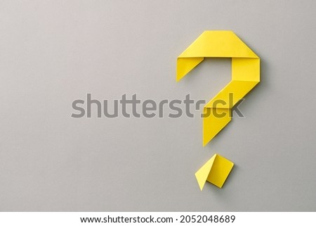 Decorative yellow paper origami question mark on grey with copy space for use as a design template