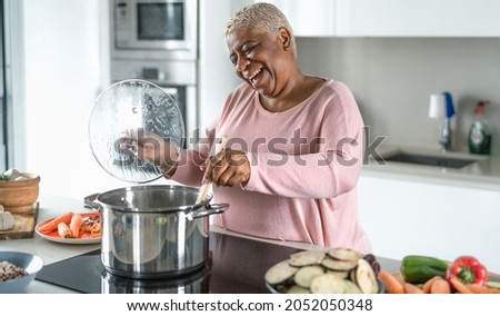 Happy senior woman having fun preparing lunch in modern kitchen - Hispanic Mother cooking for the family at home Royalty-Free Stock Photo #2052050348