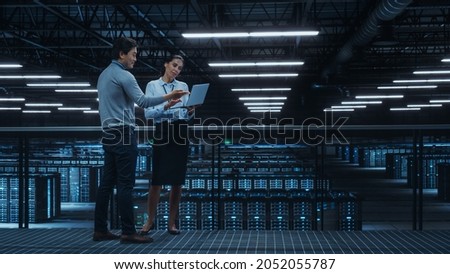 Data Center Female System Administrator and Male IT Specialist Talk, Use Laptop Computer. Information Technology Engineers work on Cyber Security Network Protection in Cloud Computing Server Farm. Royalty-Free Stock Photo #2052055787