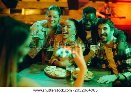 Multi-ethnic group of cheerful friends taking picture and having fun while drinking beer during their night out in a pub. 