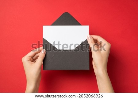 First person top view photo of hands holding open black envelope with white card on isolated red background with blank space