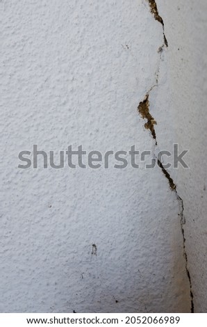 A large long crack in the white wall of a building. Cracked wall after an earthquake. Indoors. Selective focus. Close-up.