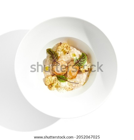 Delicious creamy risotto with sea scallop and cauliflower. Elegant main course with seafood on white plate. Grilled scallop with cauliflower and creamy rice. Seafood risotto with scallops Royalty-Free Stock Photo #2052067025