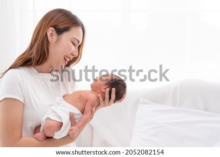 Close up portrait of beautiful young Asian mother with newborn baby. Side view of a young woman playing with her little baby in bed.