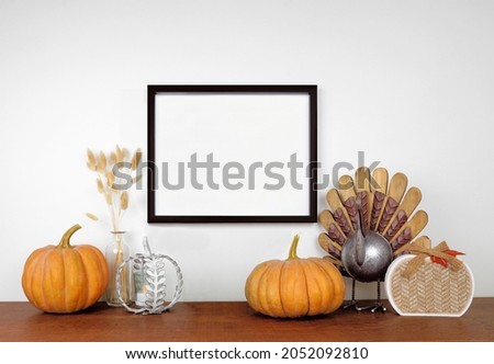 Mock up black frame hanging from a white wall with thanksgiving turkey, pumpkin and autumn decor on a wood shelf. Fall concept. Copy space.