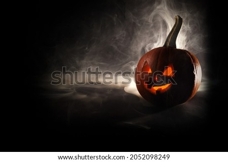 Halloween, orange pumpkin with luminous face on a blackbackground. Thick smoke comes out.
