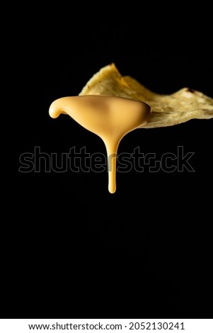 Closeup photo of a nacho with liquid cheese dripping from it on a black background Royalty-Free Stock Photo #2052130241