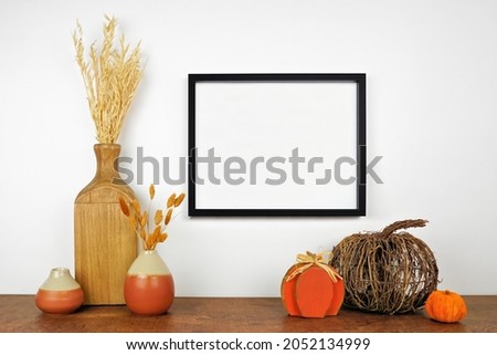 Mock up black frame hanging from a white wall with fall decor on a wood shelf. Autumn concept. Copy space.
