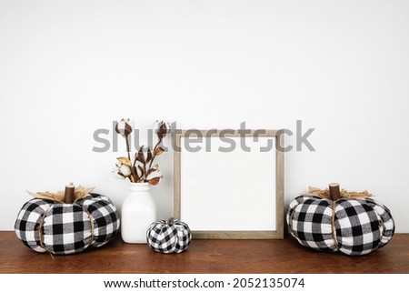 Autumn mock up. Wood frame, buffalo plaid pumpkins and fall branches on a wood shelf against a white wall. Copy space.