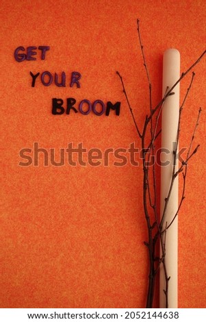 Halloween still life. A wooden stick, branches and the inscription "Take your broom" on an orange background