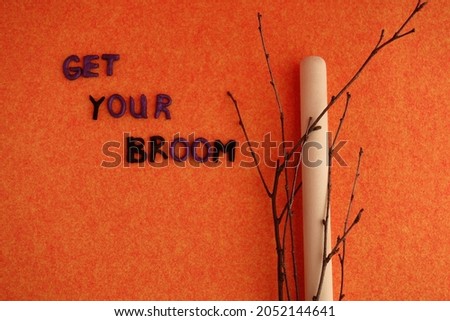 Halloween still life. A wooden stick, branches and the inscription "Take your broom" on an orange background