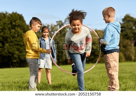 childhood, leisure and people concept - group of happy children playing game with hula hoop at park Royalty-Free Stock Photo #2052150758