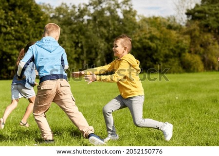 childhood, leisure and people concept - group of happy kids playing tag game and running at park