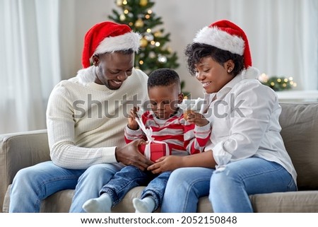 family, winter holidays and people concept - happy african american mother, father and little son opening gift box at home on christmas