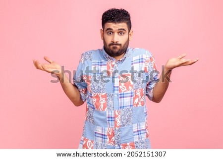 Portrait of clueless confused man in blue casual style shirt shrugging shoulders as doesn't know answer, can`t make decision, being uncertain, not sure. Indoor studio shot isolated on pink background. Royalty-Free Stock Photo #2052151307