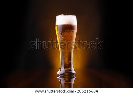 Tall glass of light beer on a dark background lit yellow Royalty-Free Stock Photo #205216684