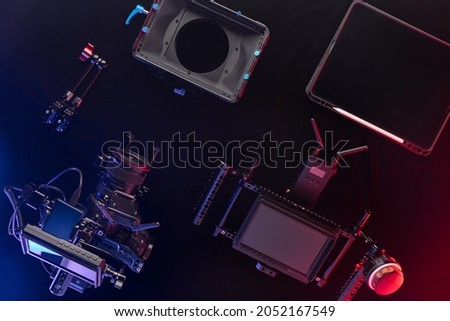 Top view of professional videographer equipment with digital camera, cage, lens and director's monitor with focus control. Top view on a black table background.