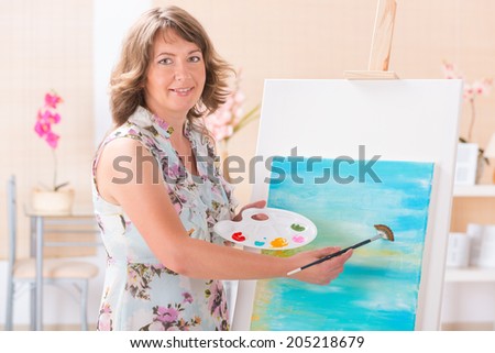 Beautiful woman painting on canvas at her home or workshop