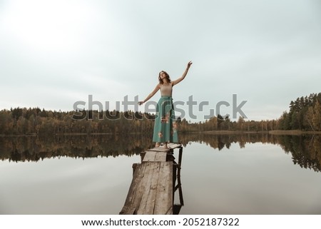 A girl is dancing on a wooden bridge against the backdrop of a forest lake.