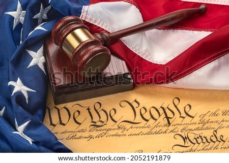 American flag draped around a judge's gavel block and the United States Constitution for use as a symbol of laws, freedom and separation of government powers.

