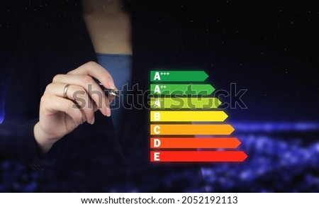 Energy efficiency concept. Hand holding digital graphic pen and drawing digital hologram energy efficiency sign on city dark blurred background. Good energy chart rating