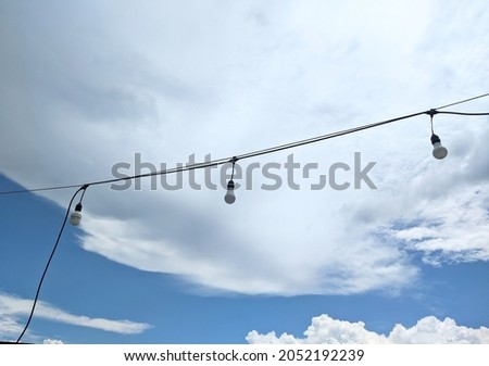 Photo of light balloons hanging on wires against the background of blue sky and clouds