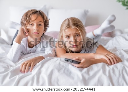 Bored tired exhausted siblings brother and sister boy and girl in pajamas lying in bedroom at home watching tv films animated cartoons