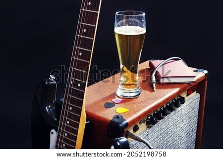 Tube combo for guitar with black guitar, glass of beer and notepad on the black background. 