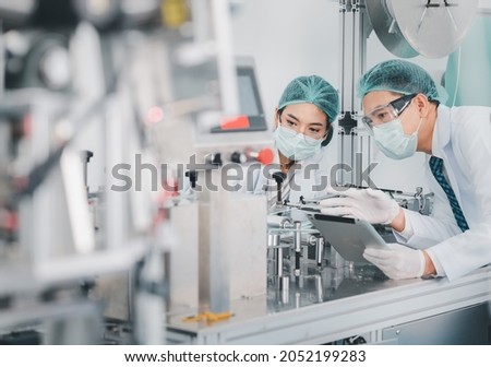 Both male and female Asian scientists are outfitted with protective gear. Examining the factory's machinery and materials used in the mask-making process. Covid 19 is a piece of preventive equipment. Royalty-Free Stock Photo #2052199283