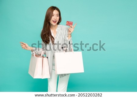 Young beautiful Asian woman smiling, showing, presenting red credit card and holding shopping bag isolated on green background Royalty-Free Stock Photo #2052203282