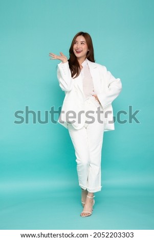 Happy Asian business woman in white suit presenting or showing open hand palm with copy space for product isolated over green background, Full body composition Royalty-Free Stock Photo #2052203303