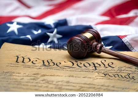 American flag draped around a judge's gavel block and the United States Constitution for use as a symbol of laws, freedom and separation of government powers.
