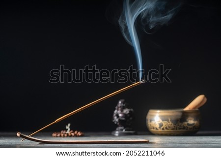 Asian incense stick in stick holder burning with smoke on black background, close up, copy space. Meditation, yoga, self development and sound therapy concept