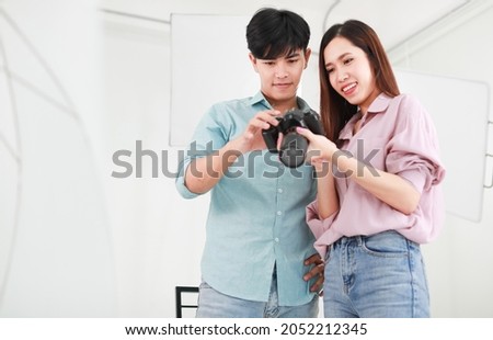 Portrait of two handsome man and beautiful woman wearing casual shirts, jeans, checking photos in camera while standing in indoor photo studio with white background cutout and lighting equipments