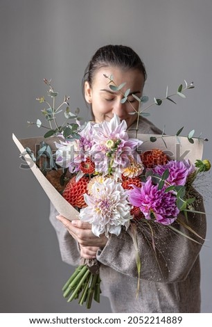 A woman holds in her hands a large festive bouquet with chrysanthemums and other flowers.
