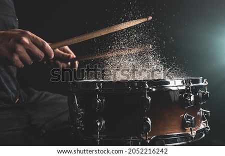 Drummer using drum sticks hitting snare drum with splashing water on black background under studio lighting close up. Royalty-Free Stock Photo #2052216242