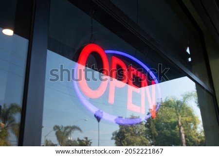 A view of a restaurant front window, featuring the a neon open sign.