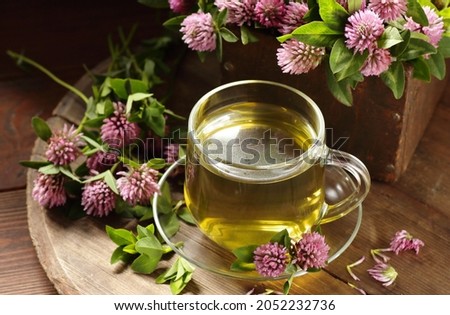 Red clover tea in glass cup on wood on rustic background, herbal drink is good for menopause, bone, heart health and for skin and hair care, closeup, naturopathy and natural medicine concept
