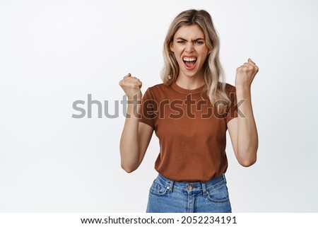 Cheerful blond woman clench fists and shouting to boost confidence, encourage herself, standing against white background