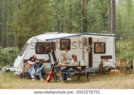 Wide angle view of young people enjoying outdoors while camping with van in forest, copy space Royalty-Free Stock Photo #2052270755
