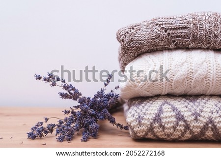 Home wardrobe with winter clothes. Woolen sweaters and dried lavender for protection from moth. Knitted warm wool clothes. Stack of warm knitted clothes with lavender. Autumn, winter season knitwear. Royalty-Free Stock Photo #2052272168