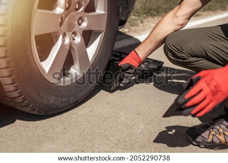 Wheel chocks under car tyre on road, man drivers hands. Royalty-Free Stock Photo #2052290738