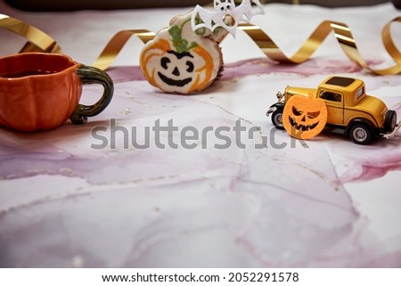 Halloween decors with orange pumpkin mug, handmade cookie, felted pumpkins and yellow retro car. Happy Halloween concept. Copy space. High quality photo. 