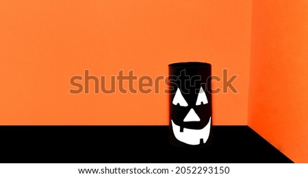 Eco-friendly black handmade Halloween decoration on table with orange background. Halloween party concept. Scary face with smile. Copy space, free text, minimalism, monochrome, banner, vintage