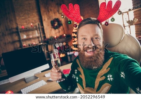 Photo of cheerful ginger guy hold glass champagne make toast wear deer headband sweater decorated office indoors