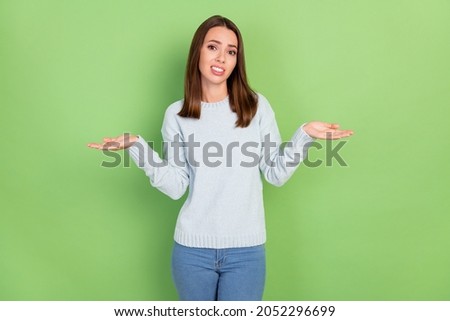 Photo of unhappy young brunette lady shrug shoulders wear blue jumper isolated on green color background