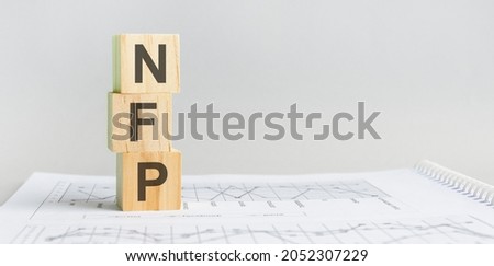 Wooden block with words NFP - acronim - net operating income. NFP wooden blocks are on the paper gray background. business concept. space for text in right. front view.